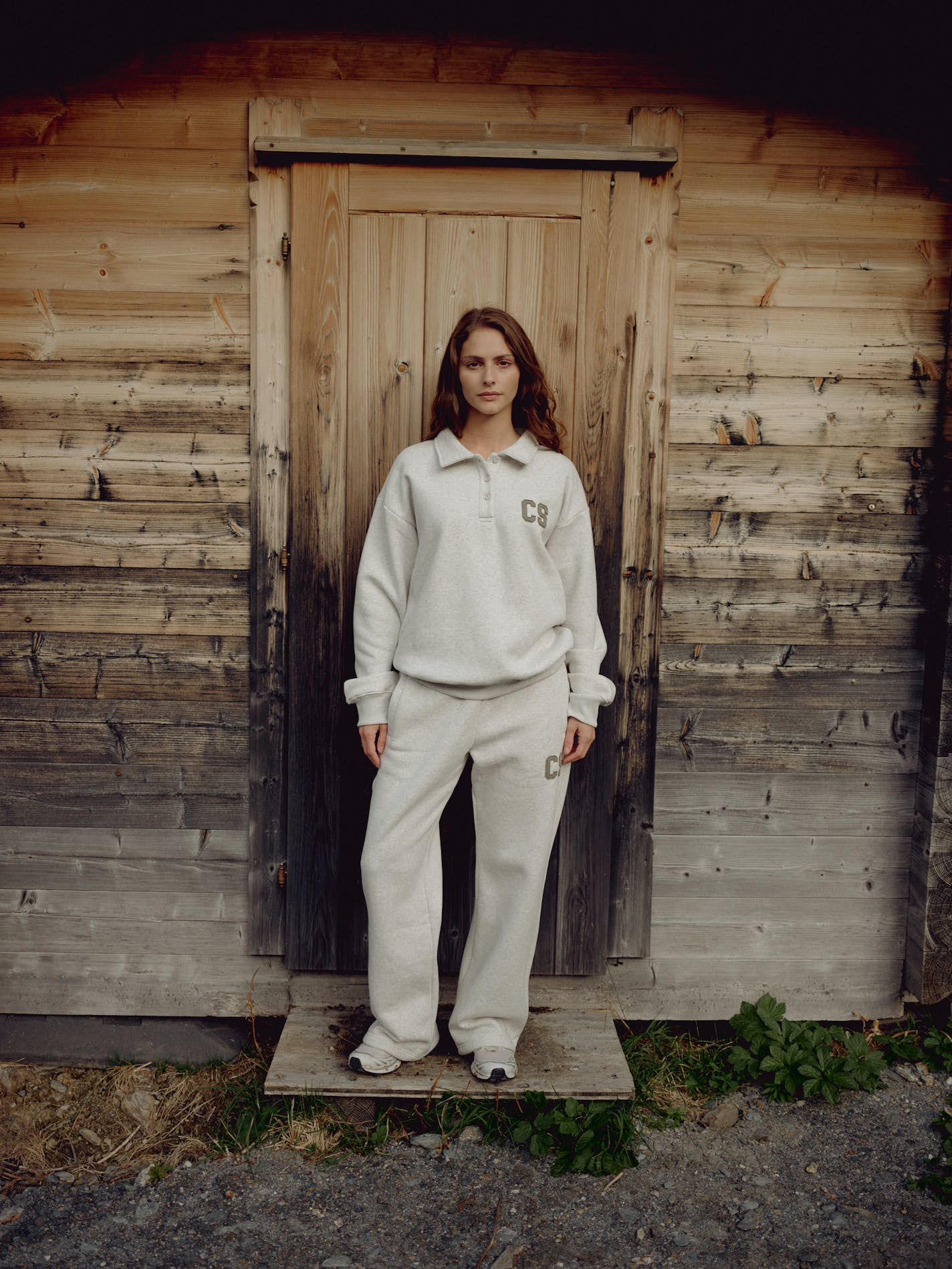 Woman wearing a grey melange CASPARA CS rugby shirt standing in front of a wooden cabin.